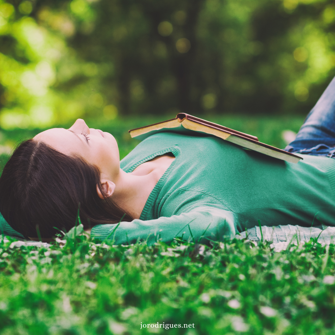 Woman lying on grass looking up. Book on chest. Resting